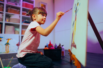 Kid Artist Painting on Easel At Home in her Studio. Little girl focusing on her artwork perfecting...