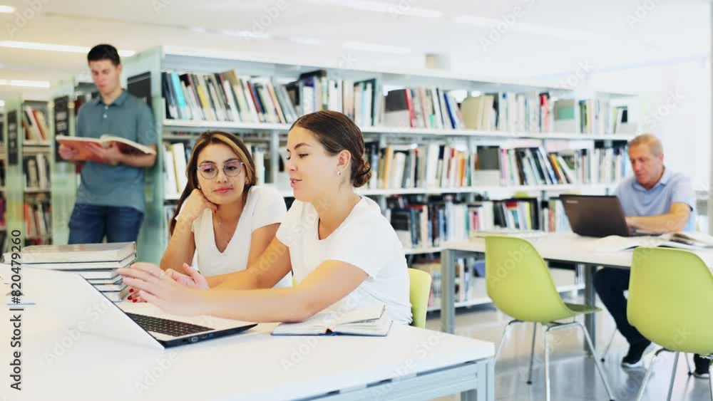 Poster two positive ladies wearing casual clothes behave loudly while studying in the library and using com