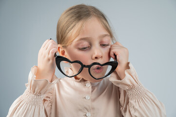 Portrait of a cute little girl blowing on heart-shaped glasses on a white background. 