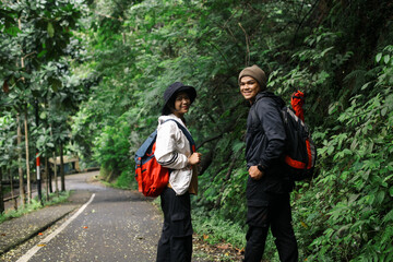 Portrait of young couple hikers with backpacks walking through the forest