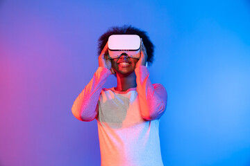 Profile thinking young beautiful African wearing VR glasses metaverse isolated on blue and pink...