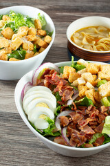 A view of a group of entrees, featuring a chopped salad, Caesar salad and chicken noodle soup.