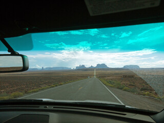 Driving by Arizona lonely desert road, approaching Monument valley, distant red rock buttes ahead, moody sky