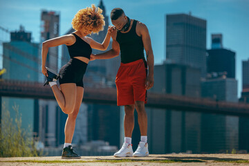A woman and a man in athletic wear stretching in an urban setting