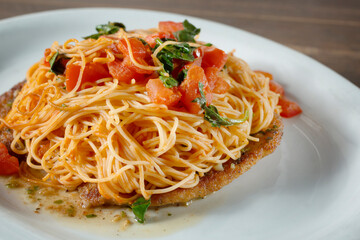 A closeup view of a dish featuring angel hair pasta and breaded chicken cutlets.