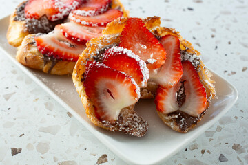 A view of croissant slices, topped with chocolate hazelnut spread and strawberries.