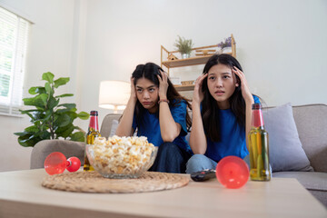 Lesbian couple anxiously watching Euro football match at home with popcorn and drinks. Concept of LGBTQ pride, sports enthusiasm, and domestic bonding