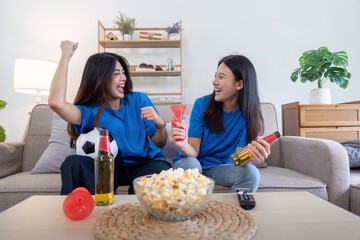 Lesbian couple cheering while watching Euro football match at home with drinks and popcorn. Concept of LGBTQ pride, sports enthusiasm, and celebration