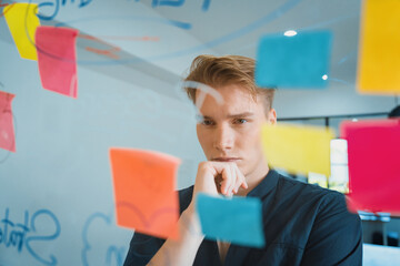 Professional caucasian businessman brainstorming marketing idea by using mind map and sticky notes on glass board at modern meeting room. Creative business and planing concept. Immaculate.