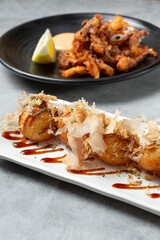 A view of a plate of takoyaki, and a plate of fried squid.