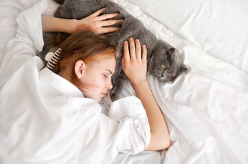 Teenager girl sleeping on white bed together with gray cat, child and pet friendship and love