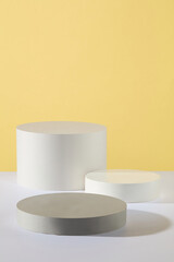 Cylinder and round shaped podiums in white and gray color are arranged against yellow background. Glamour minimal pedestal for beauty, cosmetic product presentation