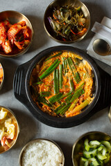 A top down view of a bowl of spicy beef soup, with several banchan bowls.