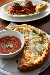 A view of a calzone entree, with a side of marinara dipping sauce.