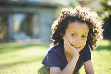 Smile, nature and portrait of child in backyard relaxing on grass for development or fun in...