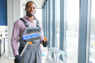 African Male professional cleaning service worker in overalls cleans the windows and shop windows...