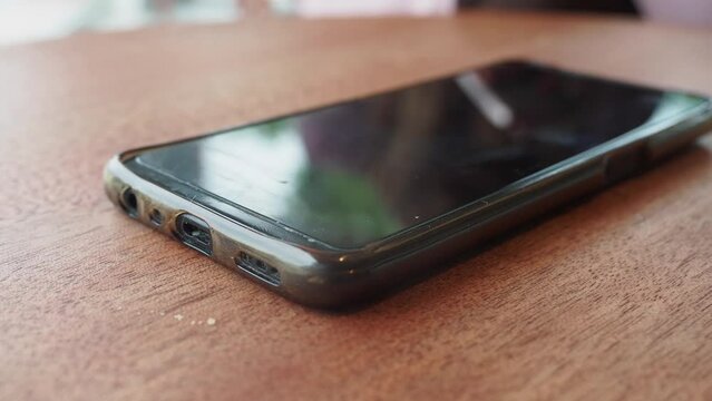 A hand grabbing and picking up mobile phone on the table.