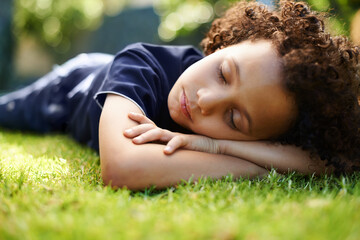 Boy, child and sleeping on lawn in garden of home for resting, exhausted and tired with dreaming in nature. Kid, fatigue and nap on grass in backyard with comfort, peace or relax for wellness outdoor