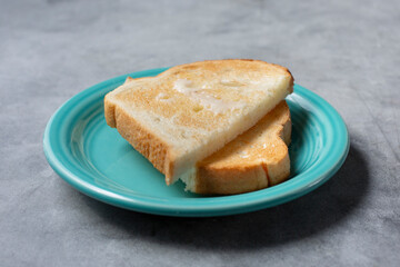 A view of a saucer of white bread toast with butter spread.