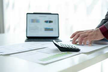 A man is using a calculator on a table with a laptop and a bunch of papers