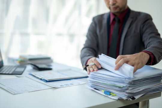 A man is sitting at a desk with a pile of papers in front of him