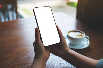 Mockup image of a woman holding mobile phone with blank desktop screen in cafe
