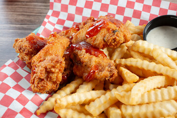 A closeup view of a basket of deep fried chicken wings with a side of crinkle cut french fries.