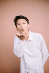 A man charmingly blowing something off his hand towards the camera, exuding charisma and confidence in a playful gesture