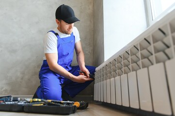 Cheerful male worker, plumber checking pipes while installing heating system in apartment