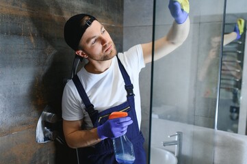 Young caucasian man in uniform cleaning a bath with steam cleaner. Cleaning service concept. Male...