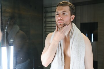 Young man looking in mirror after shaving at home