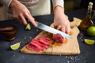 Woman cut tuna steak into slices on a wooden cutting board at domestic kitchen