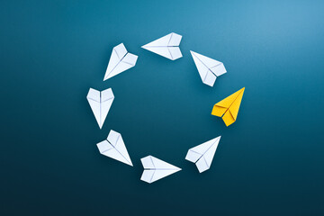 Group of white paper planes float in a circular direction and one yellow paper plane pointing in...
