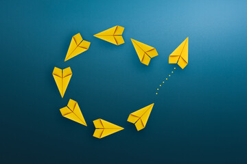 Group of yellow paper planes float in a circular direction and one paper plane pointing in...