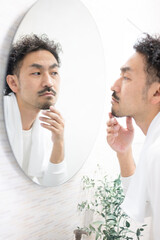 Middle-aged Japanese man with beard looking in the mirror Hair removal and morning image Men's...