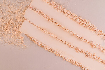 Three parallel stripes of a delicate texture of decorative face powder in a natural tone on a beige background. View from above. Swatch powder.