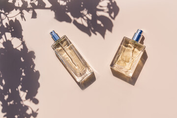 Two bottles with perfume or spray on a beige background in the rays of the sun and the shade of the leaves tree. top view. mockup. presentation