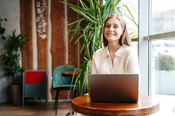 Smiling Young Woman Working on Laptop at Cozy Cafe During Daytime