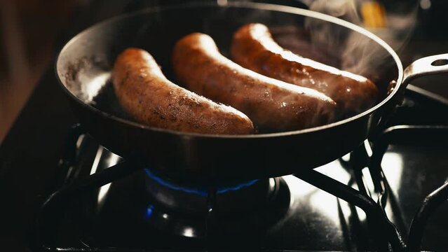Cooking three sausages on a frying pan at night 