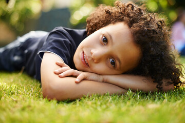 Portrait, boy child and lying on grass in outdoor park for chilling, comfort and relax in nature....