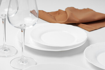 Stylish table setting with white dishware on white tablecloth