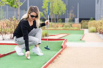 Woman playing mini golf and trying putting ball into hole. Summer leisure activity