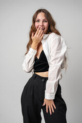 Excited Young Woman in White Blouse Reacting With Joyful Surprise Against a Grey Background