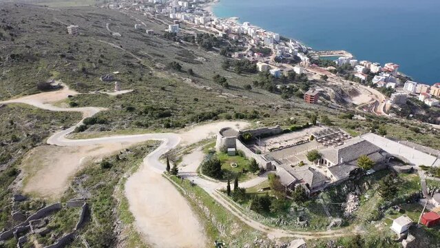 Scenic aerial view of Sarande cityscape on shores of gulf of Ionian Sea and ancient Lekuresi Castle on hill above city on sunny spring day, Albania