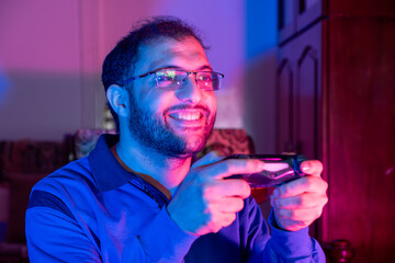 Video Gaming Concept. A Guy With Joystick Celebrating Game Win, Cheerful Man Raising Fist And Exclaiming With Excitement, Standing In Neon Light Over Purple Background.