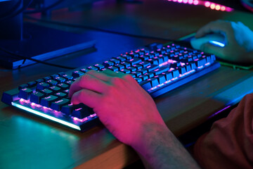 Close-up of male hands on a mechanical keyboard with RGB lights, gaming in a dark room