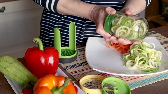 Woman pulls sliced vegetables from container of vegetable chopper in kitchen. 