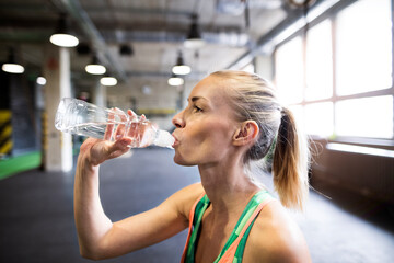 Beautiful sport woman drinking water afeter training in gym. Routine workout for woman's physical...