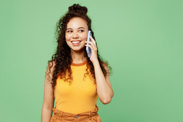 Young woman of African American ethnicity wear yellow tank shirt top talk speak on mobile cell phone conducting pleasant conversation isolated on plain pastel light green background Lifestyle concept.