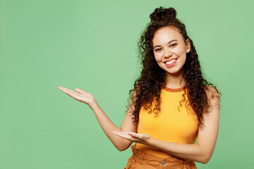 Young happy woman of African American ethnicity wears yellow tank shirt top point hands arms aside...